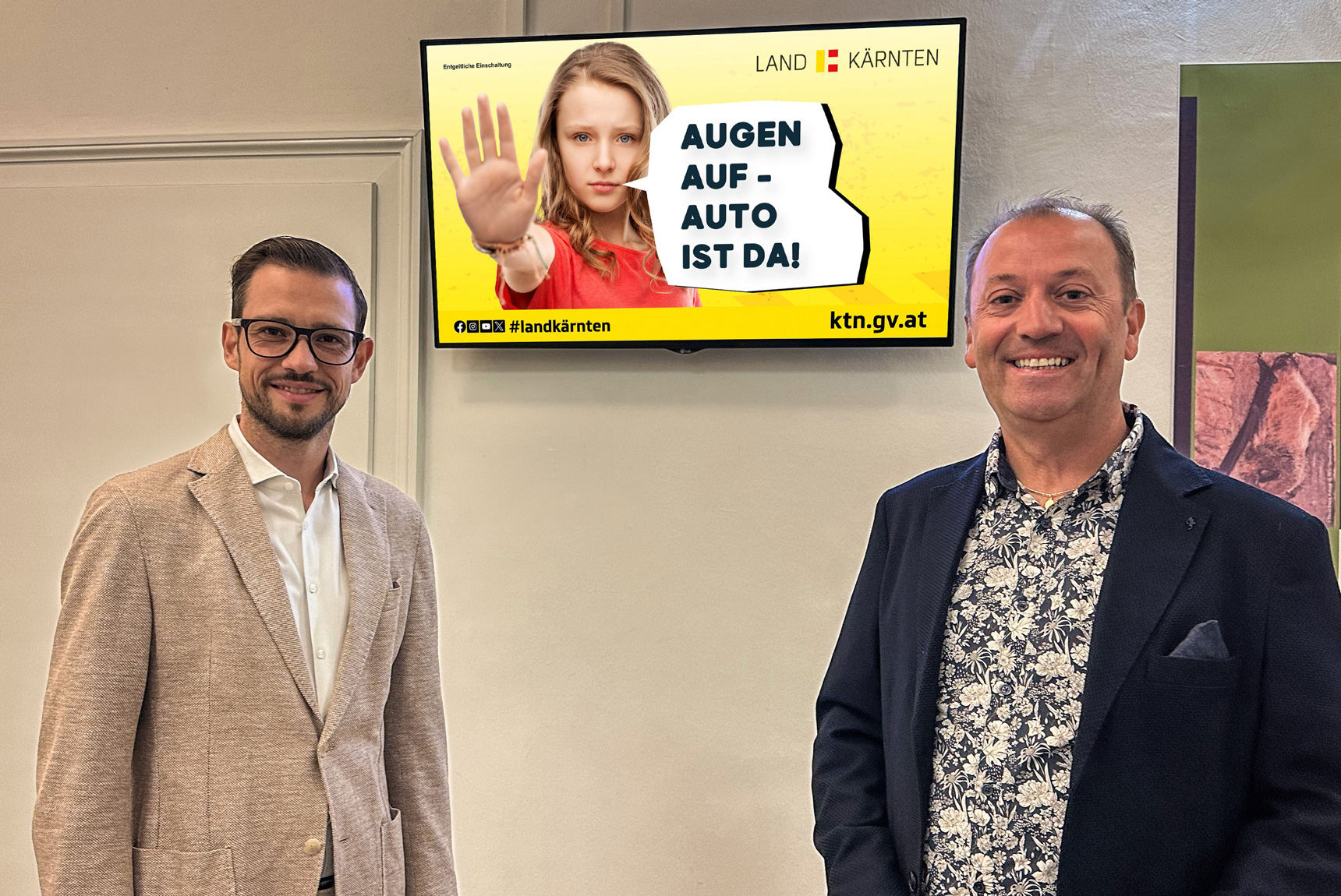 LR Sebas­ti­an Schu­sch­nig und Andre­as Lan­ner, Geschäfts­füh­rer moni­tor­wer­bung, vor einem Indoor-Screen von monitorwerbung mit den Sujet "Augen auf - Auto ist da!"