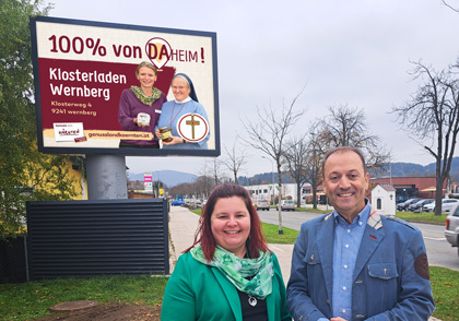 Foto von Petra Pobaschnig, Obfrau Genussland Kärnten und Auch Andreas Lanner, monitorwerbung Geschäftsführer vor einer LED Wall in Klagenfurt mit dem Sujet für Genussland Kärnten