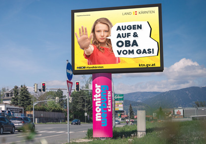 Fotomontage von Grafik Land Kärnten Sicherer Schulweg mit Slogan "Augen auf & Oba vom Gas" auf der LED-Wall Villach Süd von monitorwerbung